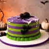Pastel de Halloween a rayas moradas y verdes decorado con telarañas dulces y arañas negras 3D en CDMX